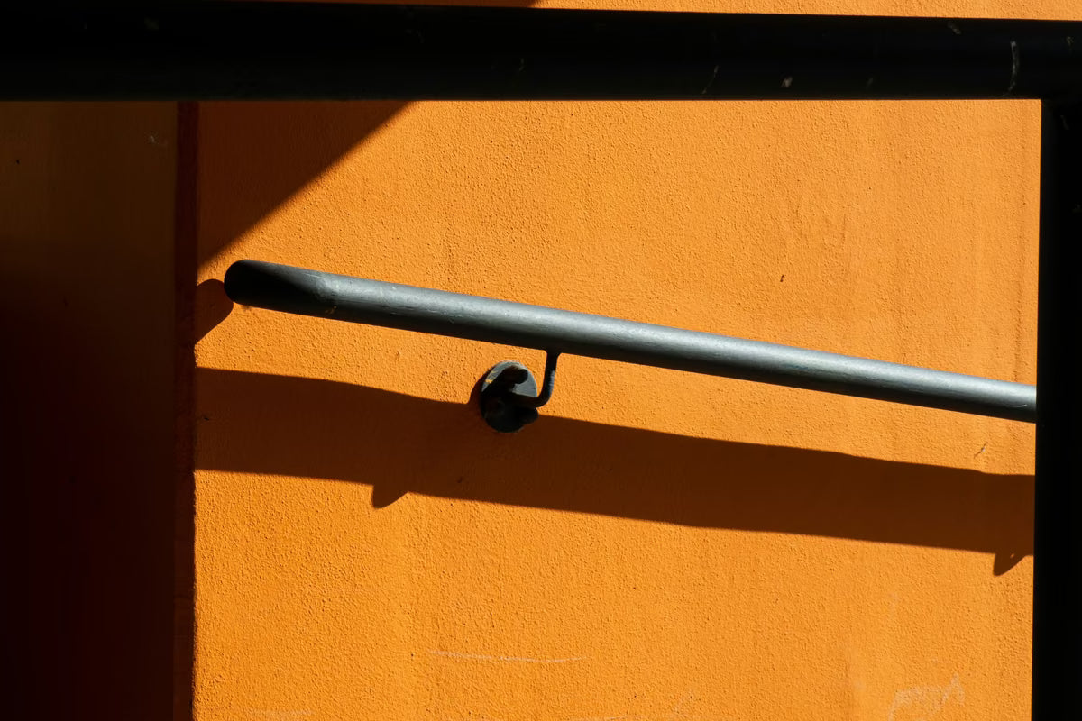 Barra de apoio de metal fixada em parede laranja com sombra