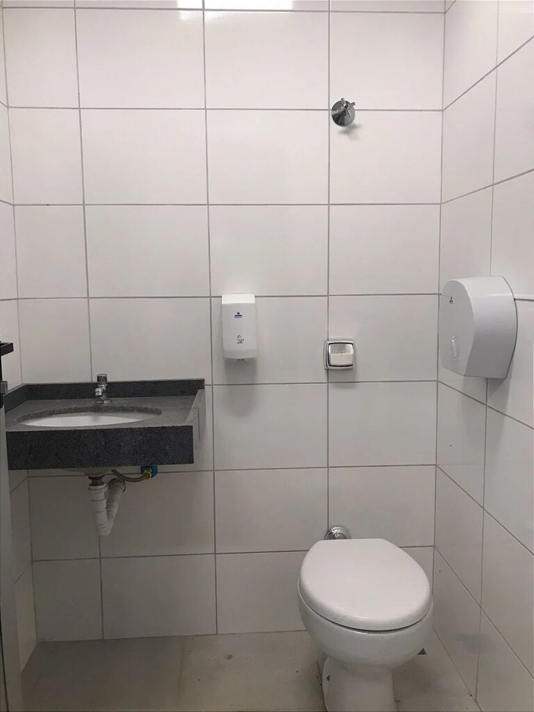 Banheiro escolar com lavatório em granito, torneira de acionamento e dispensadores de papel toalha e higiênico fixado...