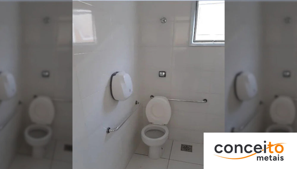 Banheiro adaptado com barra de apoio horizontal ao lado do vaso sanitário, dispensador de papel e piso com ralo, segu...