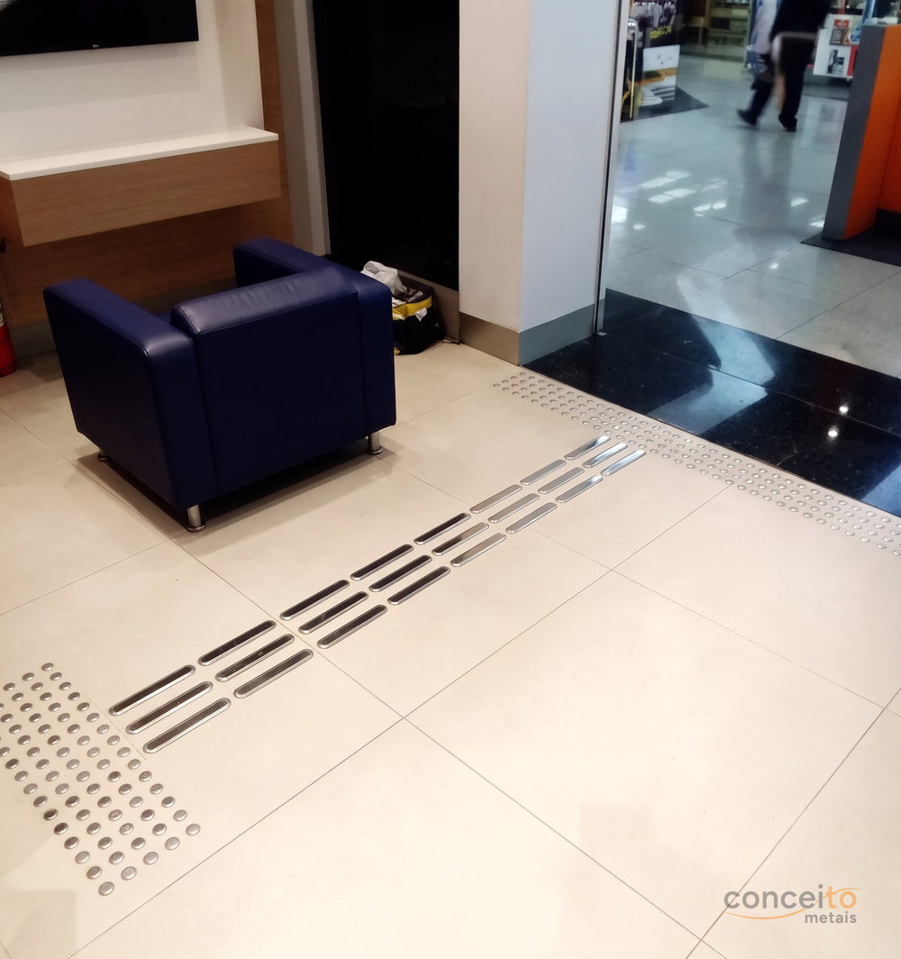 Piso tátil direcional conduzindo até a entrada da loja, com piso tátil de alerta na transição para a área externa em ...