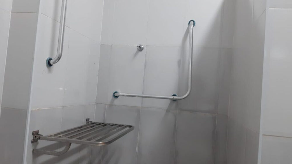 Box de chuveiro com barra de apoio em L instalada em inox e gancho de parede, além de banco articulado retrátil na po...