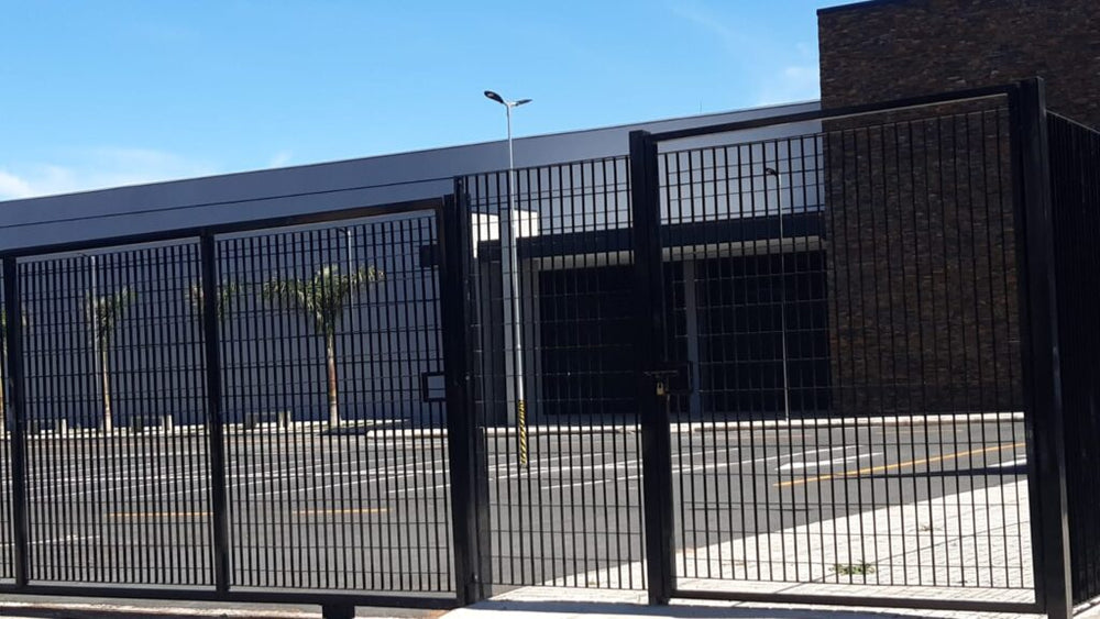 Portão de acesso em grade metálica do Pavilhão da Viber, com pátio pavimentado e paisagismo de palmeiras na entrada. ...
