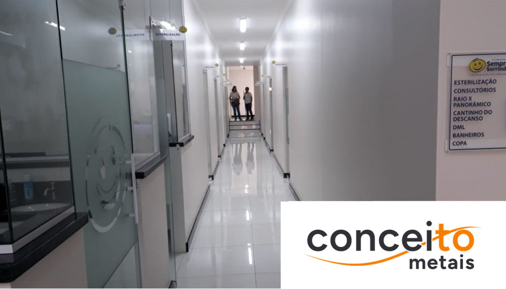 Corredor de acesso aos consultórios da clínica, com portas de vidro identificadas e piso em porcelanato branco de fác...