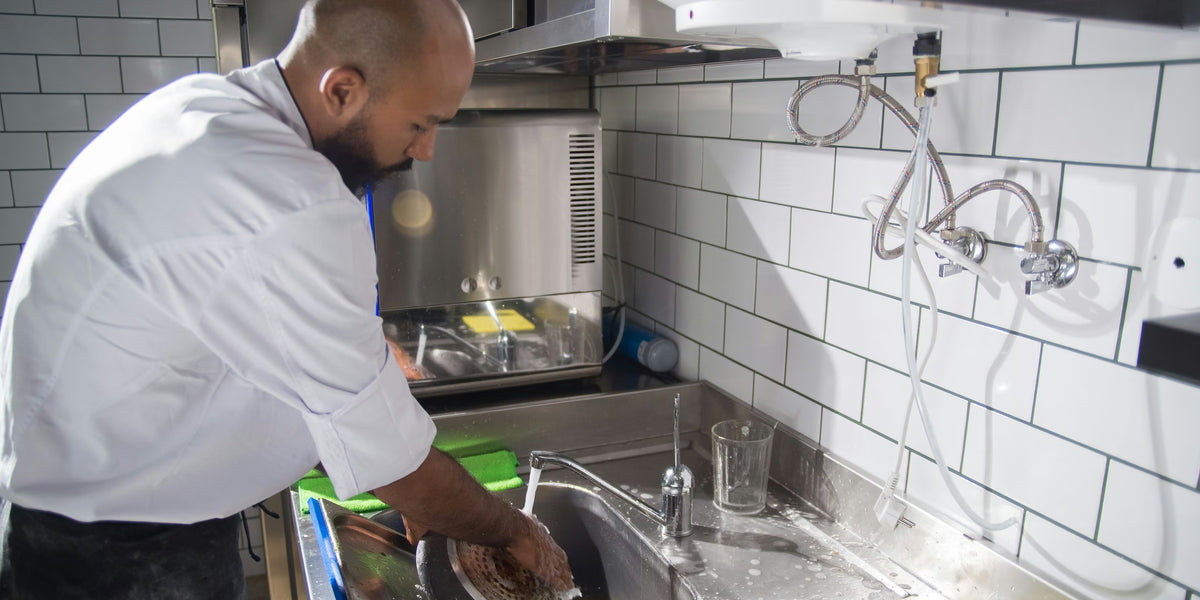 Profissional lavando utensílios em pia de aço inox de cozinha profissional